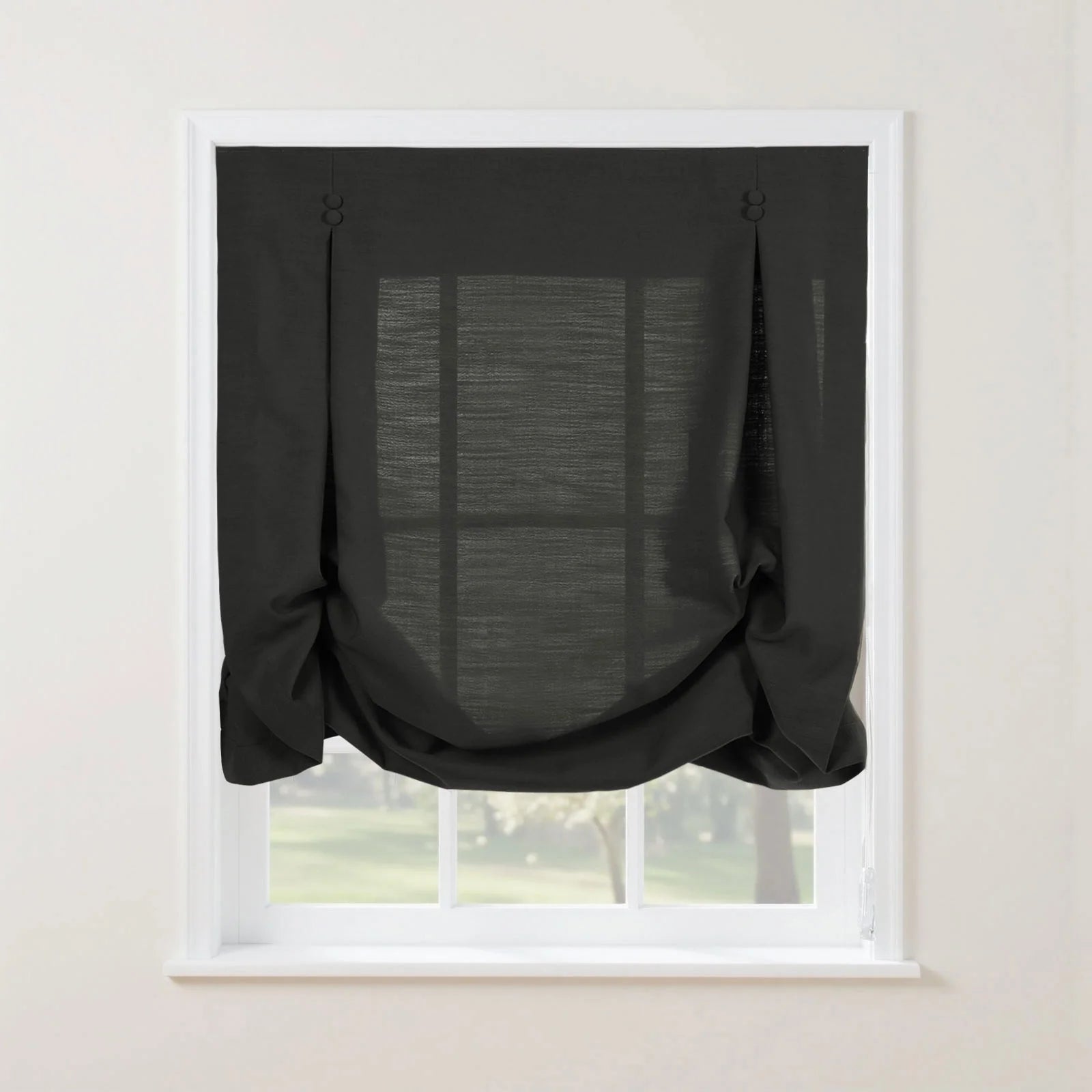 Dark charcoal linen-look tie-up curtain with decorative buttoned loops at the top and a softly gathered bottom on a white window frame overlooking a lush green outdoor view