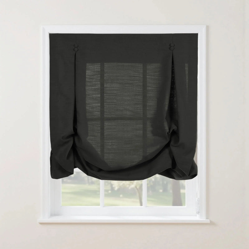 Dark charcoal linen-look tie-up curtain with decorative buttoned loops at the top and a softly gathered bottom on a white window frame overlooking a lush green outdoor view