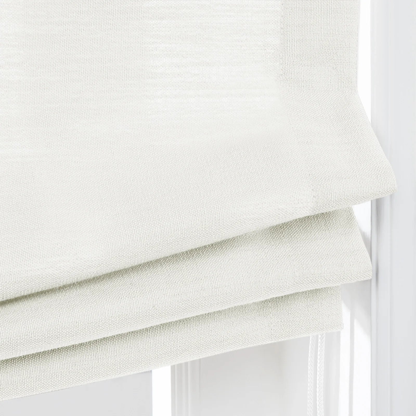 Photograph of textured off-white Roman blinds with three horizontal folds and braided pull cords hanging in a window