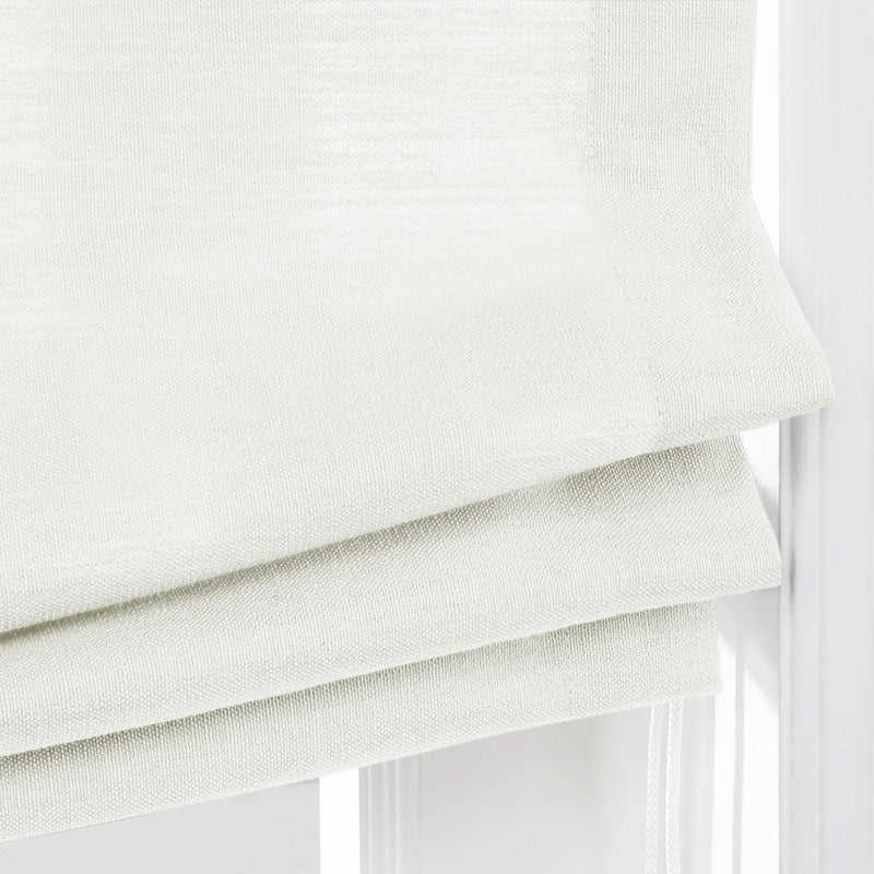 Photograph of textured off-white Roman blinds with three horizontal folds and braided pull cords hanging in a window