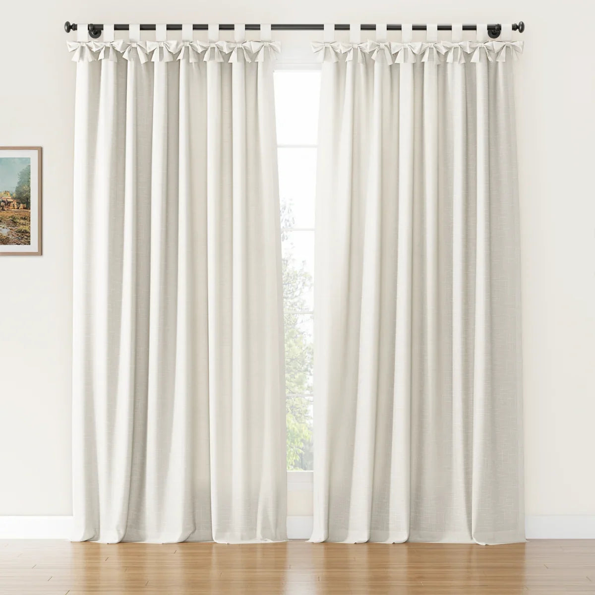 Off-white linen-look tie-top curtains featuring decorative bows on a black rod in a bright room with a warm wooden floor and a glimpse of a small framed landscape painting