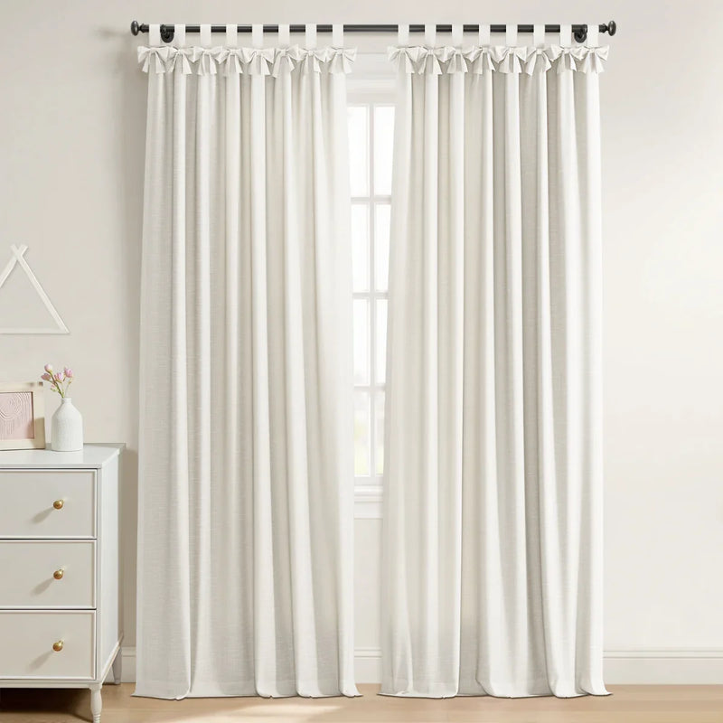 White linen-blend tie-top curtains on a black rod in a bright room, next to a white three-drawer dresser with brass pulls and pink flowers