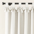 A cream linen-textured curtain with decorative bow-tie top tabs hangs from a black curtain rod with a round finial