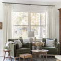 Ivory White Liz Linen Pleated Curtains beside a green sofa, table lamps and nested coffee tables