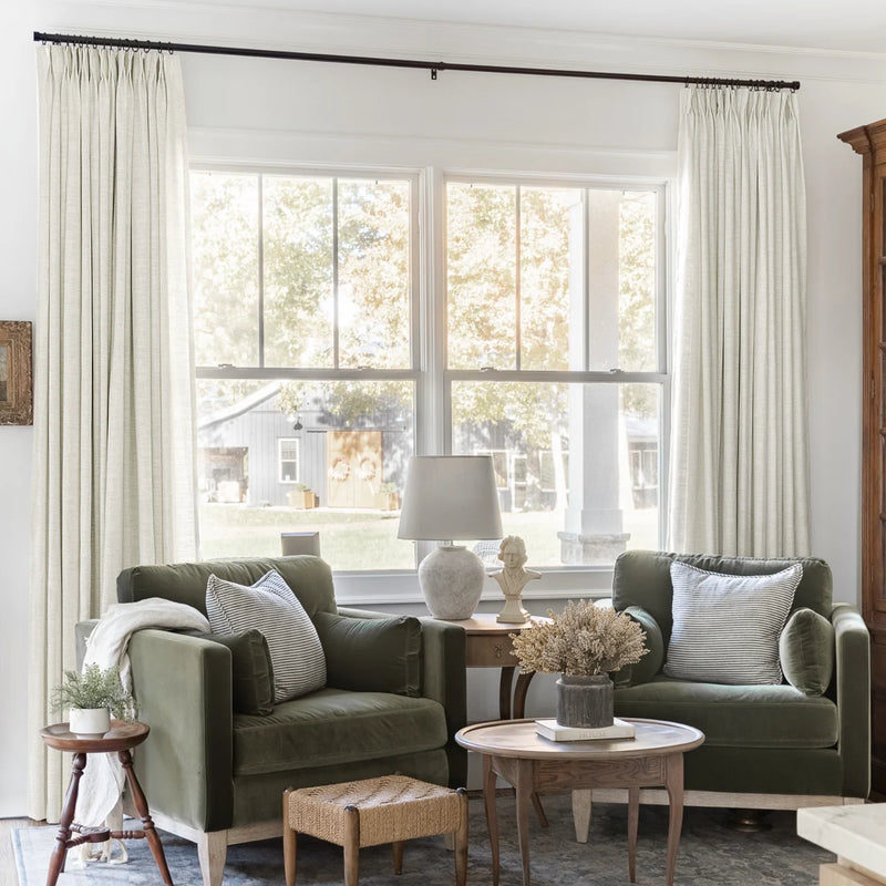 Ivory White Liz Linen Pleated Curtains beside a green sofa, table lamps and nested coffee tables