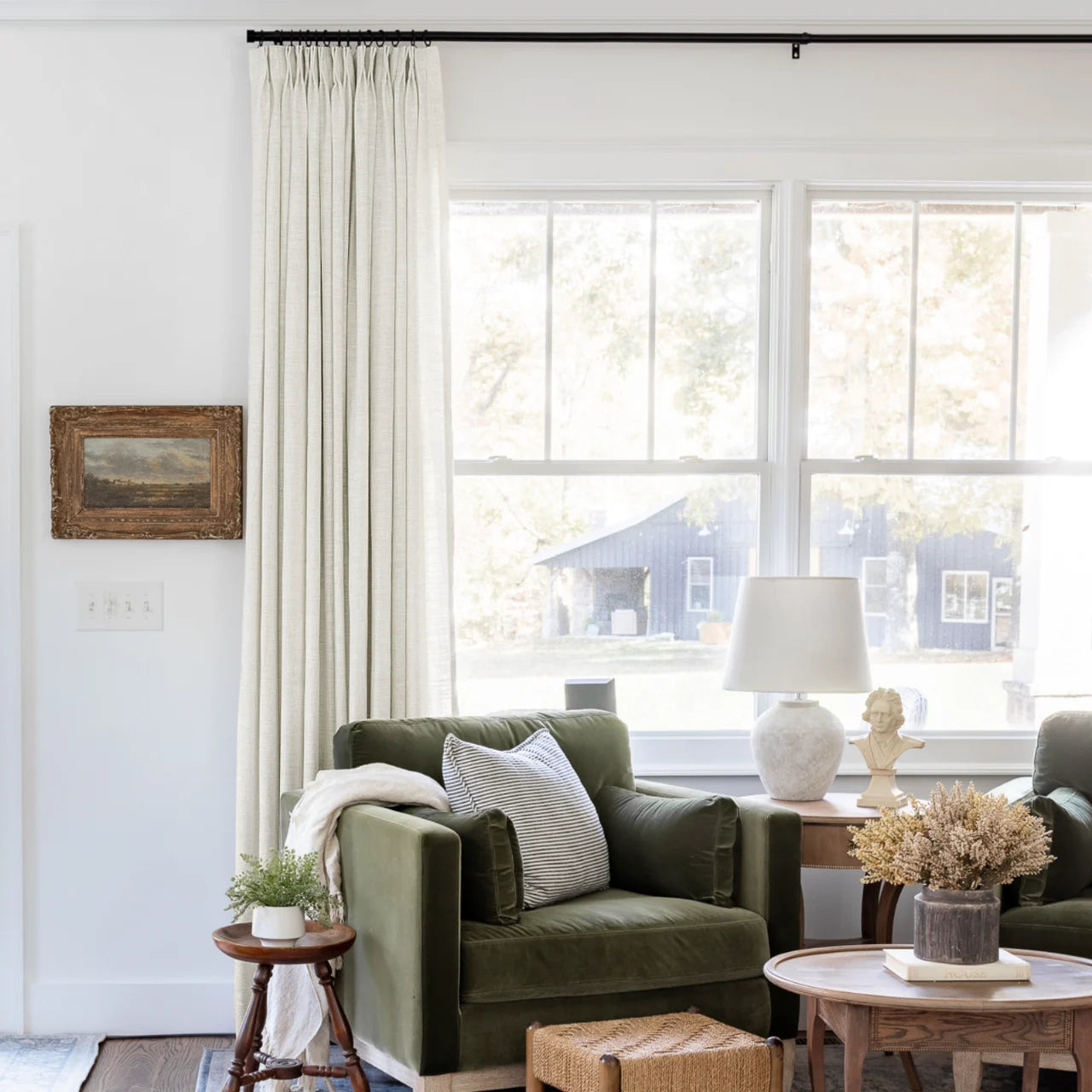 Ivory White Liz Linen Pleated Curtains framing a green sofa beneath a wide sunlit window