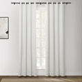 Photograph of a modern interior with a window dressed in white blackout curtains featuring black grommets and rod, an abstract white and black framed artwork on the left wall, and a light brown textured rug on a dark wood floor