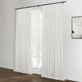 White pleated drapes on a black rod covering a multi-pane window with green foliage outside, a dark wood floor, and an abstract black and white framed artwork on the right wall