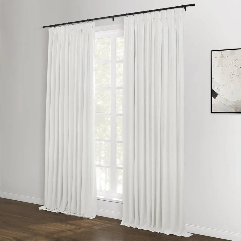 White pleated drapes on a black rod covering a multi-pane window with green foliage outside, a dark wood floor, and an abstract black and white framed artwork on the right wall