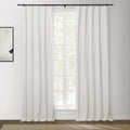 Photograph of a brightly lit interior window featuring white blackout curtains on a black rod, an abstract white and black artwork on the left wall, and a patterned brown rug on a hardwood floor