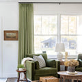 Jade Green Olive Liz linen curtains shown closer beside a sunlit window with smooth vertical folds