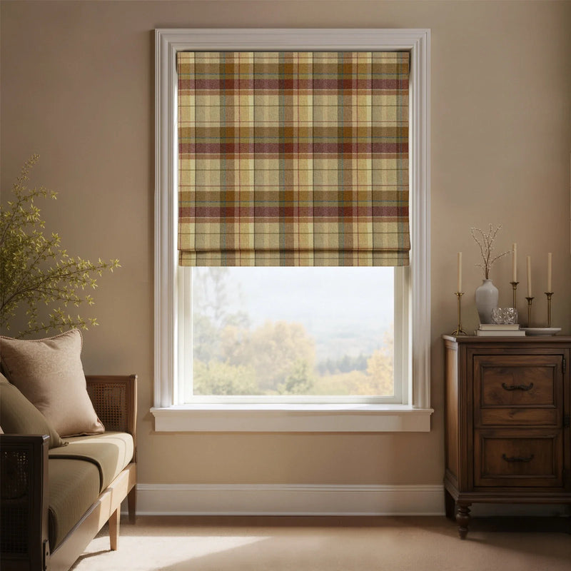 Interior room with a window featuring a beige, brown, and red plaid Roman blind, a dark wood dresser with brass candlesticks and a light gray vase of dry branches, and a beige daybed overlooking a hazy rural landscape