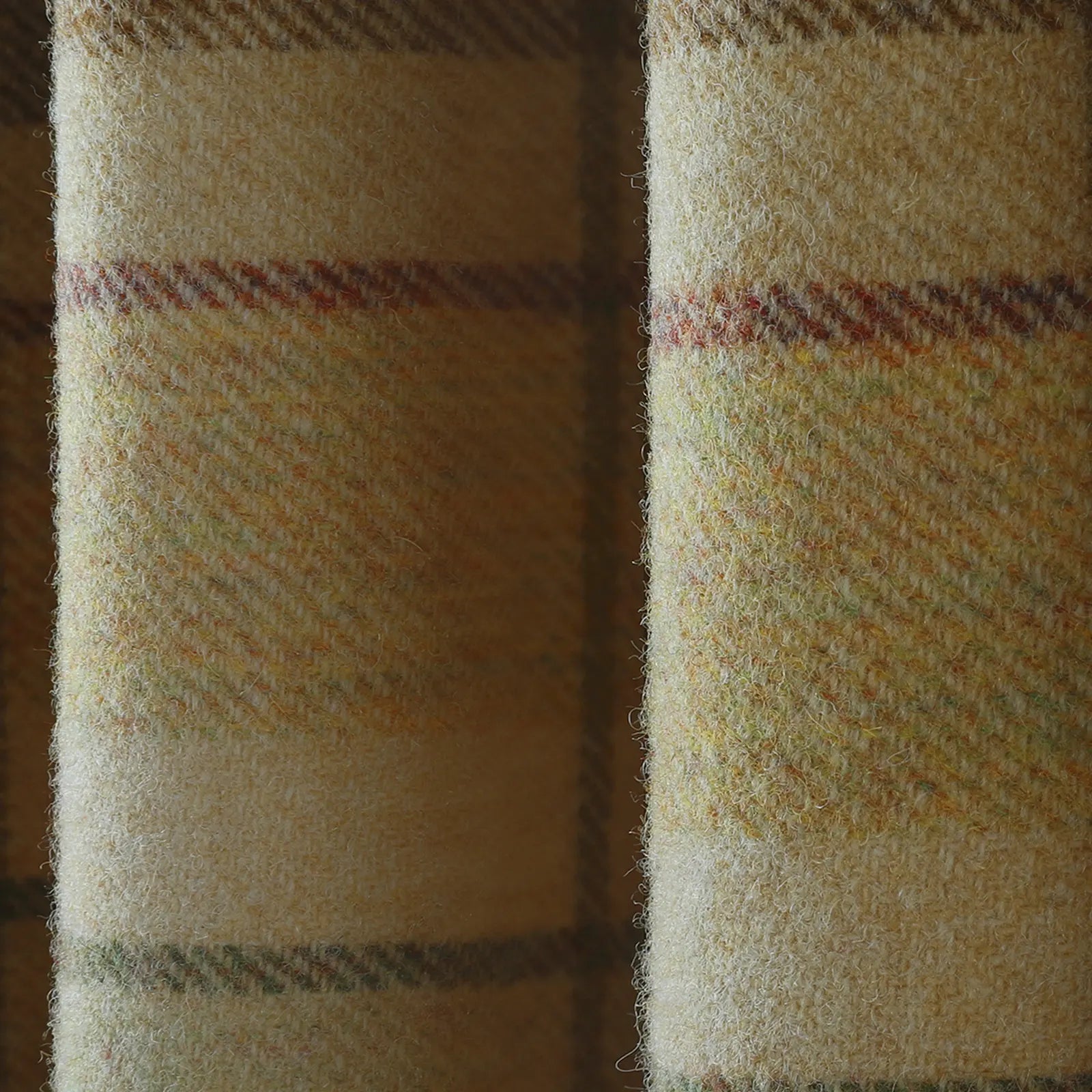 Wool fabric detail of a muted cream and beige tweed with a fuzzy nap, showcasing subtle plaid lines in reddish-brown, olive green, and dull yellow