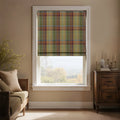 An inviting room with a window featuring a colorful plaid Roman blind in muted red, green, and gold tartan, offering a scenic autumnal landscape view, complemented by a light wood daybed and a dark antique cabinet with candles