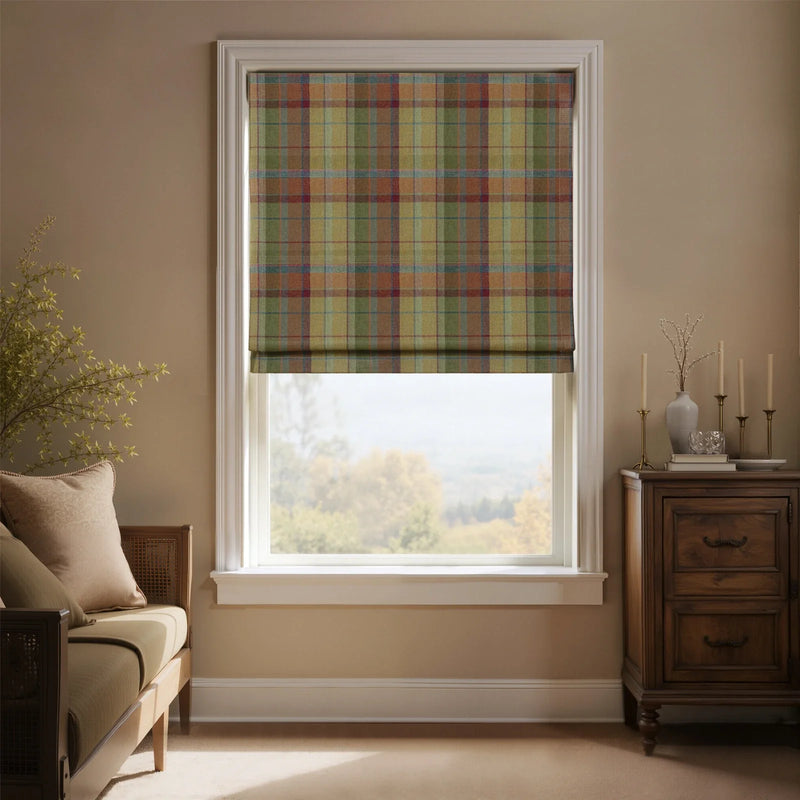 An inviting room with a window featuring a colorful plaid Roman blind in muted red, green, and gold tartan, offering a scenic autumnal landscape view, complemented by a light wood daybed and a dark antique cabinet with candles
