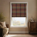 Interior shot of a cozy room featuring a window with a red, green, and brown tartan plaid Roman blind overlooking a distant autumn landscape, a wood daybed with neutral cushions, and a dark antique cabinet decorated with brass candlesticks