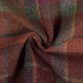Wool tartan fabric featuring a rustic plaid pattern of deep maroon, forest green, subtle yellow, and fuchsia lines, draped in soft folds with a prominent central swirl