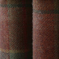 Close-up of rustic red-brown woolen fabric with a fuzzy texture and subtle green and yellow plaid pattern separated by a dark central fold