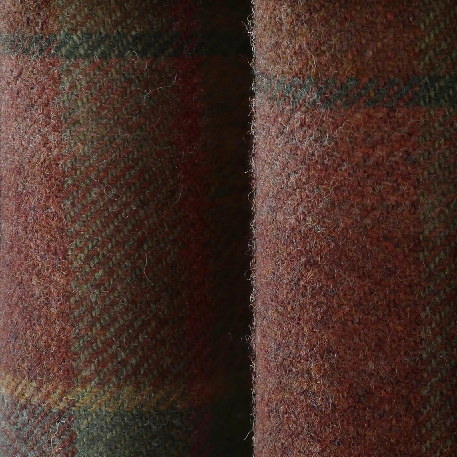 Close-up of rustic red-brown woolen fabric with a fuzzy texture and subtle green and yellow plaid pattern separated by a dark central fold