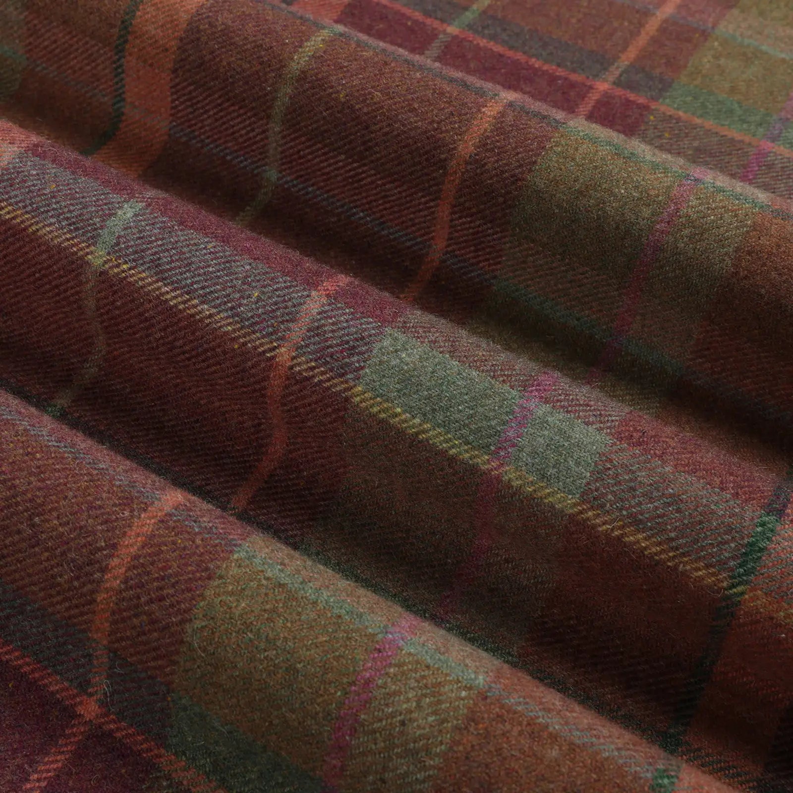 Woven wool fabric displaying a rustic tartan plaid pattern in deep burgundy and forest green with subtle orange yellow and magenta lines highlighting its textured folds