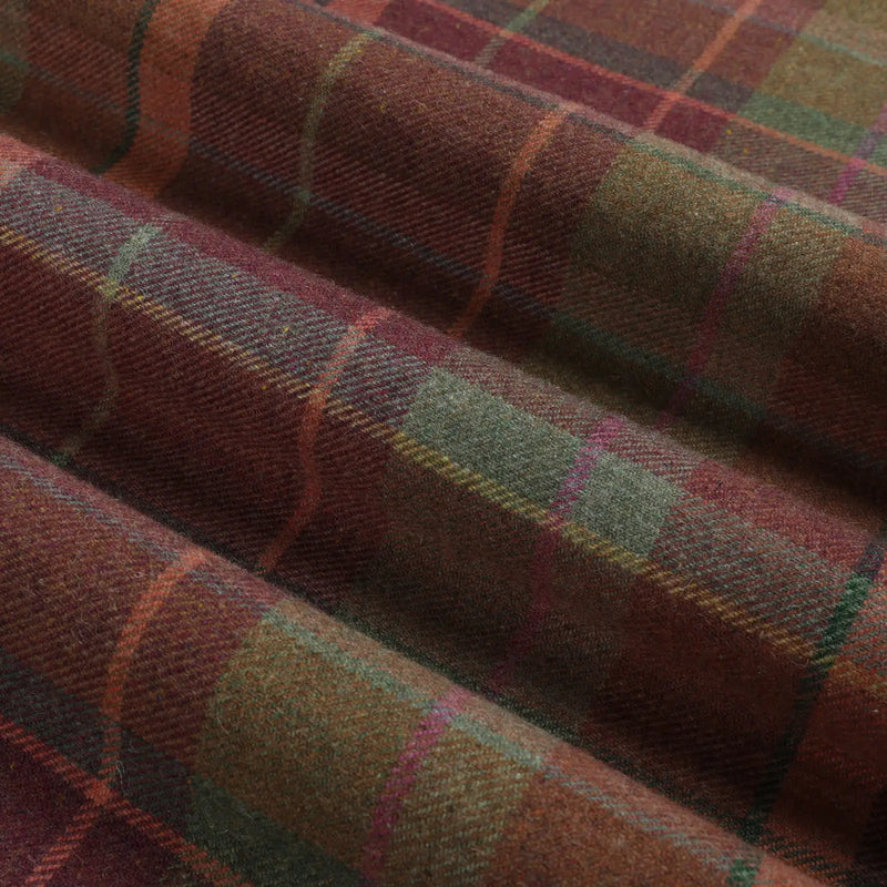 Woven wool fabric displaying a rustic tartan plaid pattern in deep burgundy and forest green with subtle orange yellow and magenta lines highlighting its textured folds