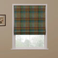 A fabric Roman blind with a multi-tonal tartan plaid pattern in earthy greens, browns, blues, and subtle red lines, partially lowered to reveal a pleated bottom edge in a window setting