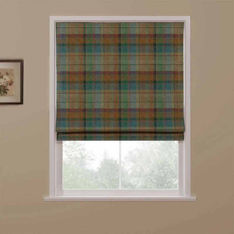 A fabric Roman blind with a multi-tonal tartan plaid pattern in earthy greens, browns, blues, and subtle red lines, partially lowered to reveal a pleated bottom edge in a window setting