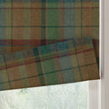 A partially lowered window blind of textured woolly tartan fabric in earthy greens and browns with thin red and teal lines