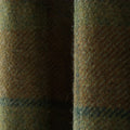 Photograph of a close-up textured wool tweed fabric in earthy olive green, brown, and hints of dark blue, featuring a prominent vertical fold and visible fuzzy surface fibers