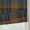 A textured Roman blind in a vibrant plaid pattern of teal, mustard, and maroon hues with visible white stitching partially covering a window