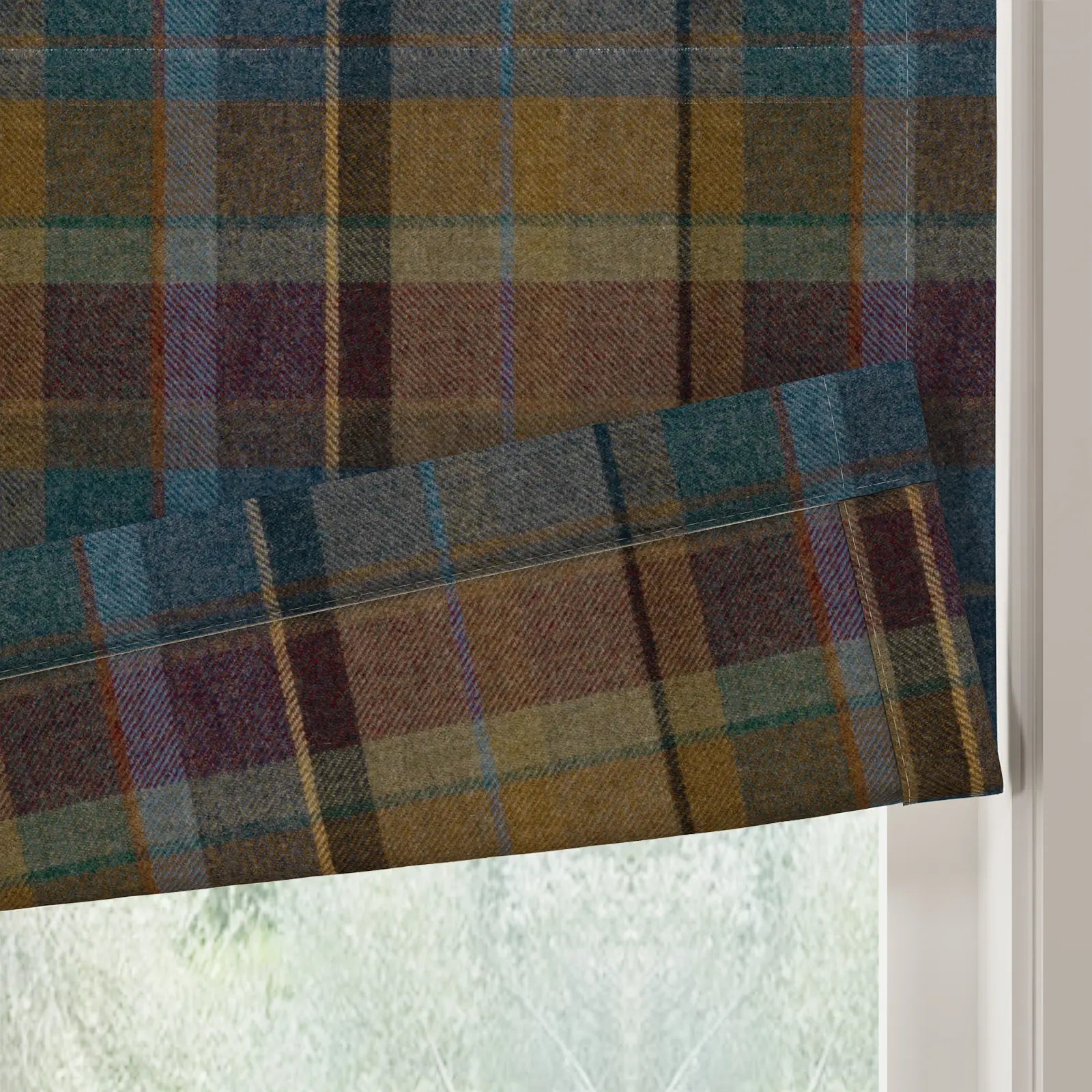 A textured Roman blind in a vibrant plaid pattern of teal, mustard, and maroon hues with visible white stitching partially covering a window