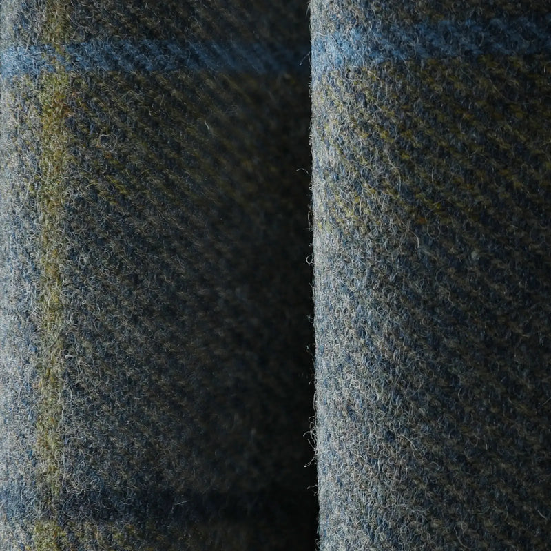 A close-up of folded dark grey-blue wool fabric with visible textures, featuring subtle olive green and light blue threads woven throughout