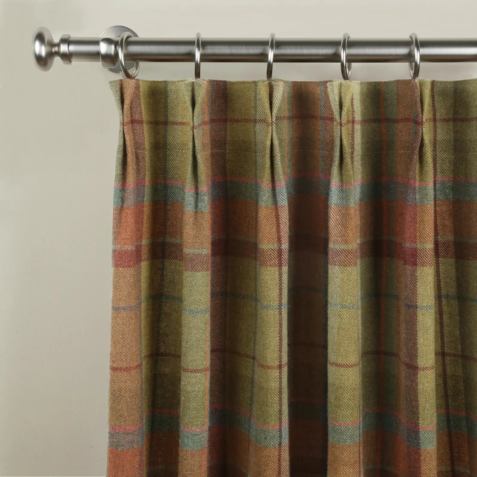 Photograph of a pleated plaid curtain featuring earthy olive green, rust, and brown tones accented with subtle pink and blue lines, suspended from a brushed nickel curtain rod
