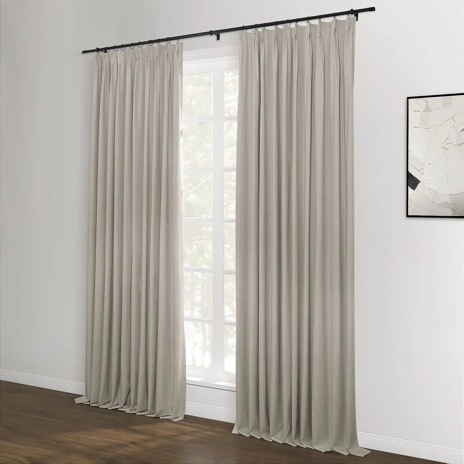 Beige pleated curtains on a black rod flank a large white window in a contemporary room featuring a dark wood floor and a minimalist black and white abstract artwork