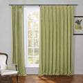 Sage green pleated curtains draped beside a white paned window offering a view of a lush forest complemented by an ornate cream armchair and a framed lemon botanical print