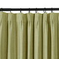 A close-up of a sage green textured curtain with pinch pleats hanging from a black rod with rings