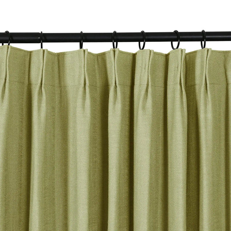 A close-up of a sage green textured curtain with pinch pleats hanging from a black rod with rings