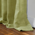 Lime green woven linen curtain fabric with visible texture elegantly draped and pooling on a rich dark wood floor beside a clean white baseboard