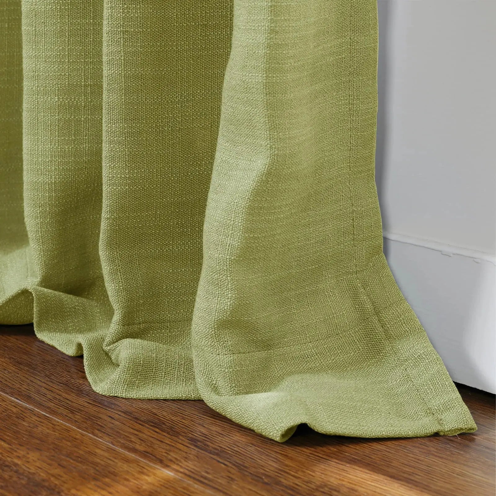 Lime green woven linen curtain fabric with visible texture elegantly draped and pooling on a rich dark wood floor beside a clean white baseboard