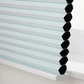 Close-up photograph of a light blue cellular window Blind featuring visible black honeycomb cells resting on a white windowsill