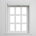 A white-framed window with nine blank panes, featuring a partially rolled-up light blue-grey Blind, and intricate white wooden trim against a clean wall