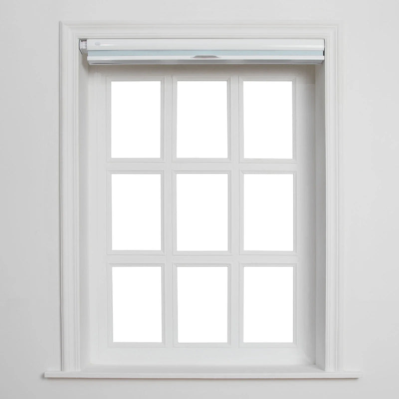 A white-framed window with nine blank panes, featuring a partially rolled-up light blue-grey Blind, and intricate white wooden trim against a clean wall