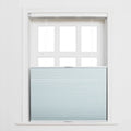 Photograph of a white framed window with a light blue cellular top-down bottom-up Blind featuring subtle horizontal stripes and visible white pull cords, revealing the upper six panes
