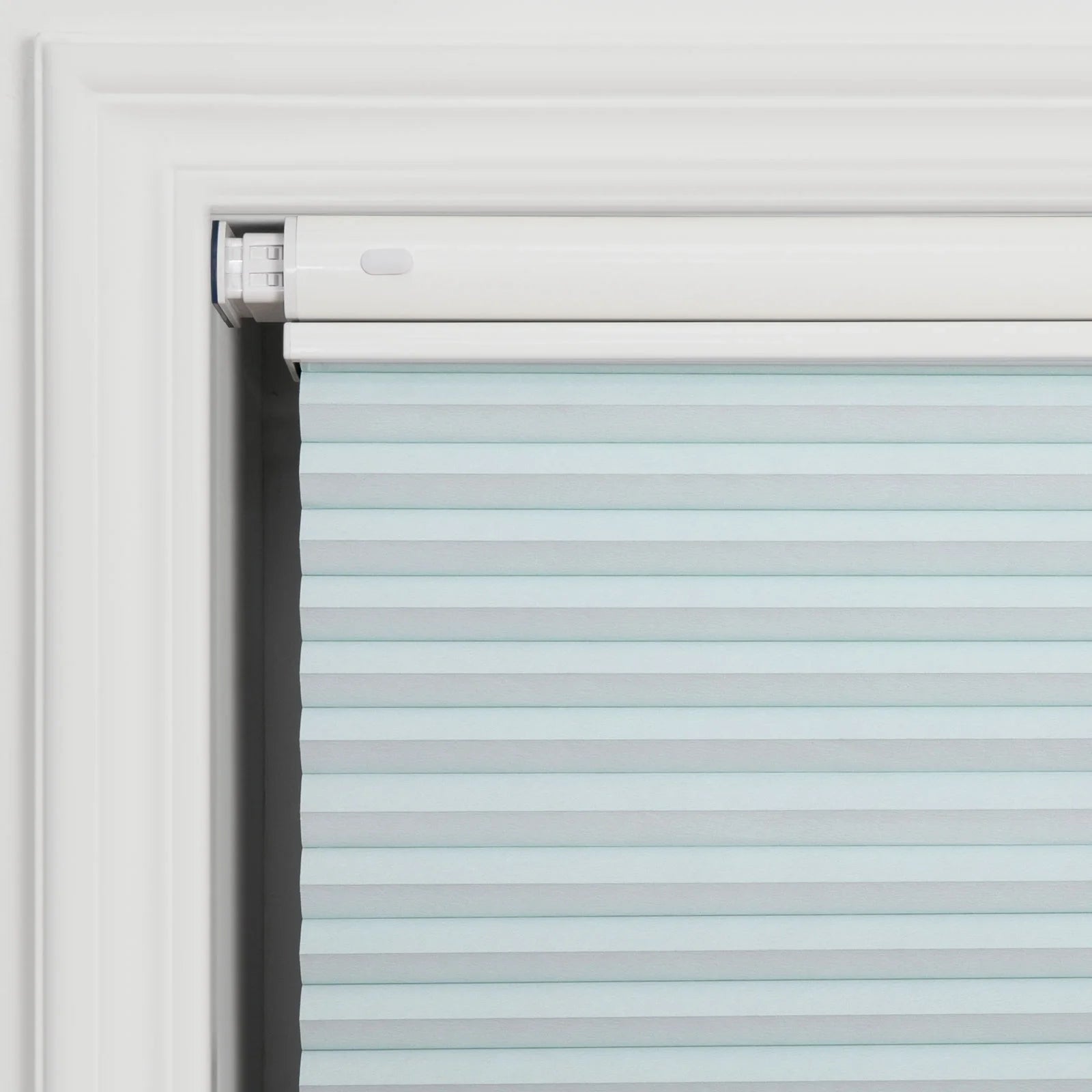 Photograph of a pale blue cellular pleated window Blind installed within a white decorative window frame showing its clean white headrail with a subtle oval adjustment button