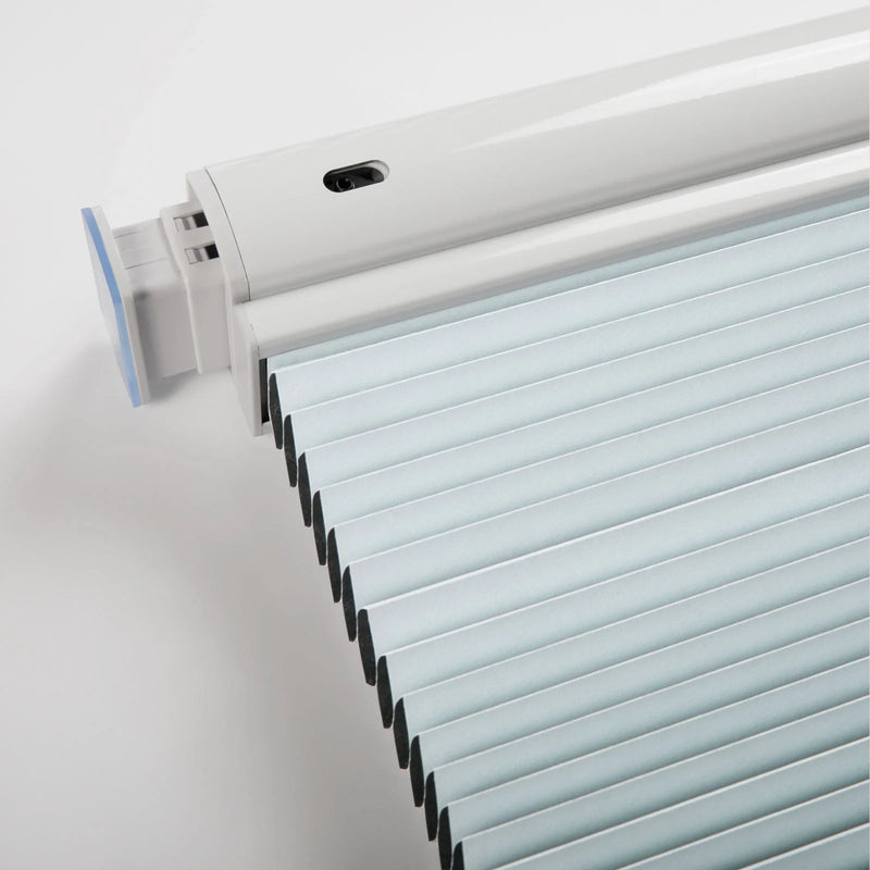 Close-up of a modern white motorized pleated window Blind system with light blue fabric pleats a black sensor on the headrail and a translucent blue end cap