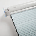 Digital photography of a modern window Blind mechanism in a studio showcasing a white headrail with an oval button, light blue pleated fabric Blinds, and a translucent blue end cap