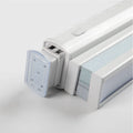 Close-up of a white modern window Blind headrail featuring a clear plastic end cap with mounting holes, a small gray control button on its top surface, and compressed light blue and gray pleated fabric