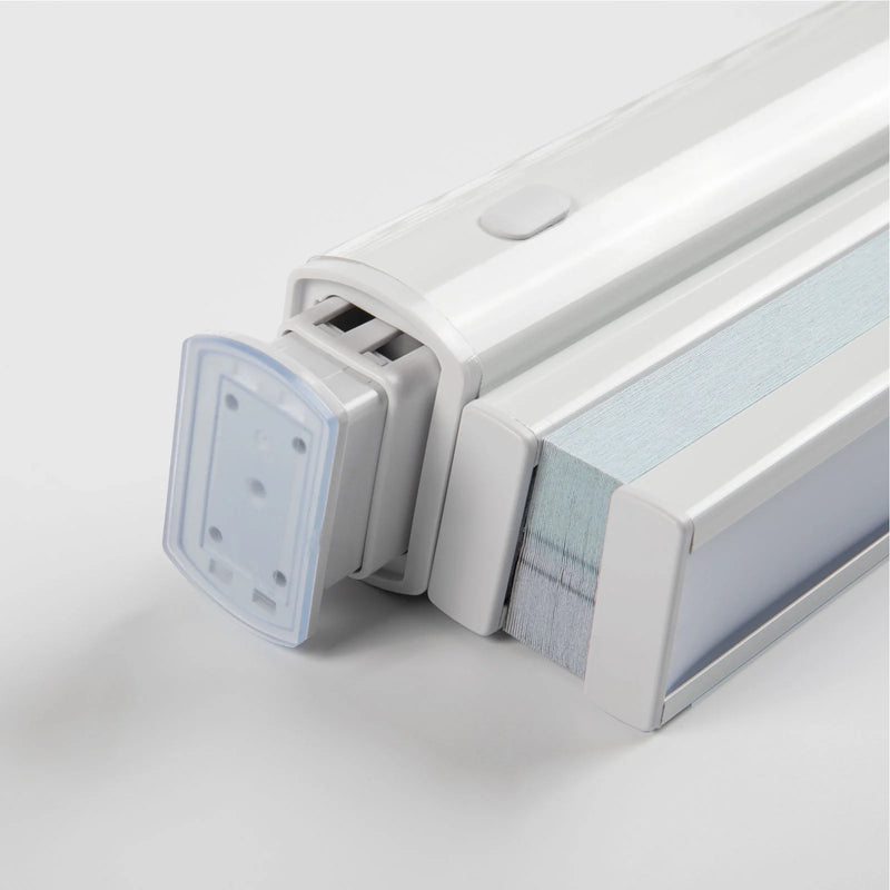 Close-up of a white modern window Blind headrail featuring a clear plastic end cap with mounting holes, a small gray control button on its top surface, and compressed light blue and gray pleated fabric