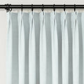Photograph of light blue-grey textured pinch pleat curtains on a black rod with rings