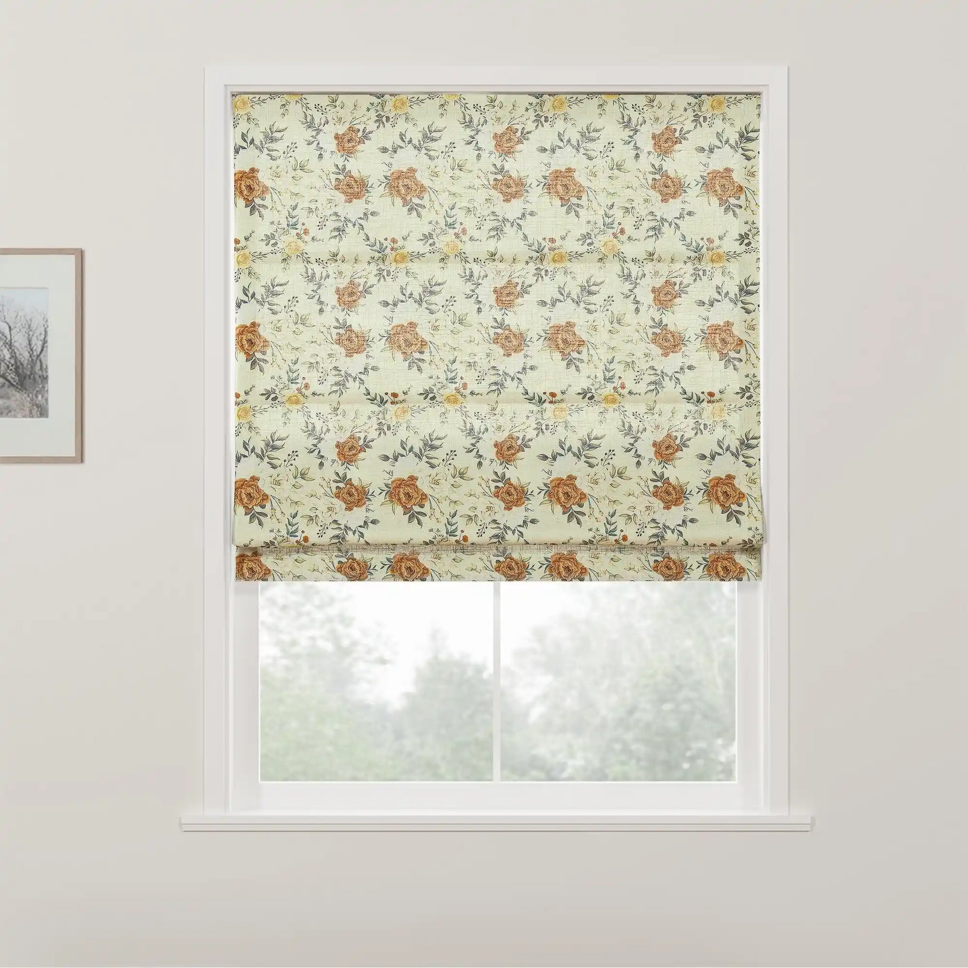 A Roman blind with a light cream background and an intricate floral pattern of rust orange roses yellow flowers and grey-green leaves hangs in a white-framed window overlooking blurred green foliage